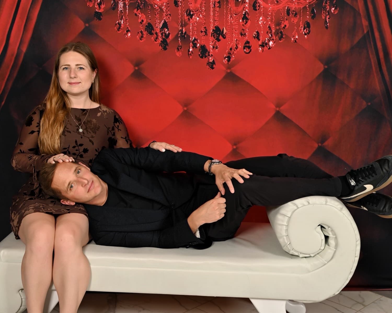 Thomas and Victoria posing playfully together against a red lounge backdrop.
